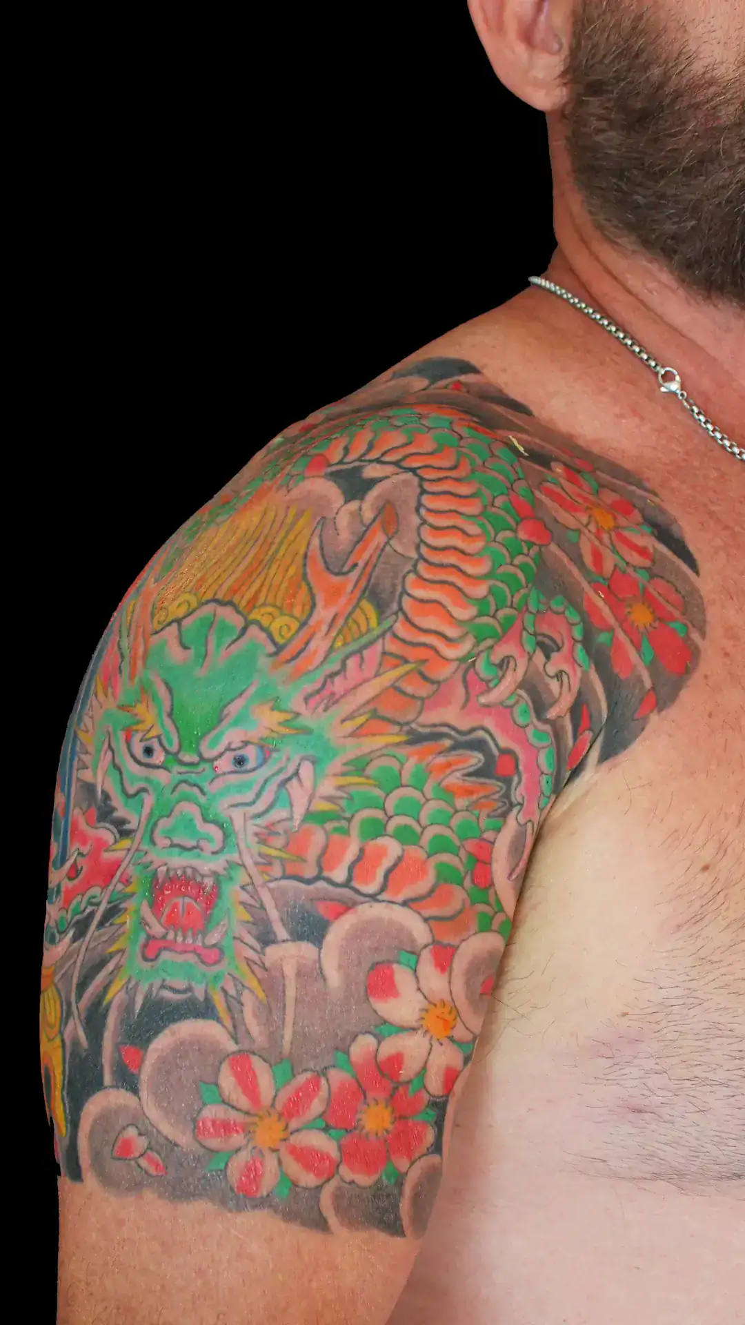 Irezumi de dragón verde con escamas naranjas y flores tradicionales, tatuaje japonés en hombro y brazo por Nikko Quiroga.