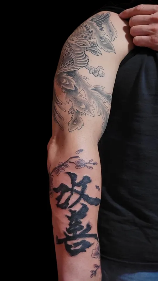 Tatuaje japonés que muestra los Kanji 放 (hō / hanasu) y 喜 (ki / yorokobu), junto a un fénix. Tatuaje realizado por Nikko Quiroga en manga de hombro.