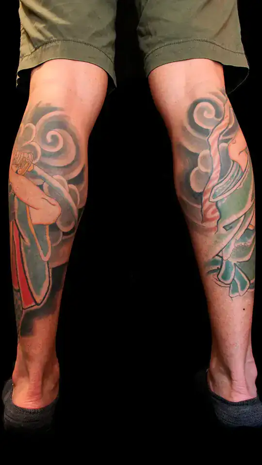 Vista posterior de tatuaje japonés con Musashi Miyamoto y Sasaki Kojirou en cada gemelo, rodeados de nubes en estilo irezumi tradicional.