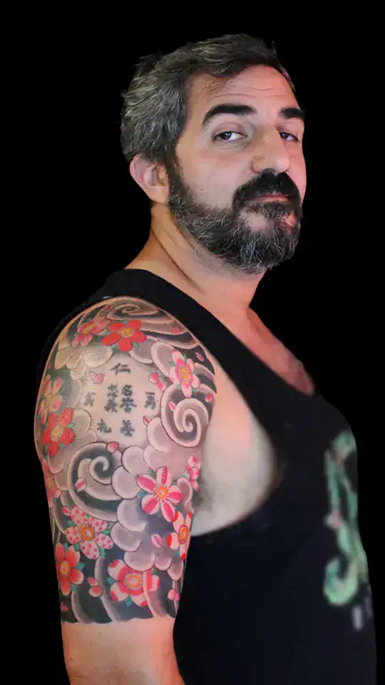 Tatuaje japonés de flores de cerezo y caracteres kanji en manga de brazo y hombro, con fondo de nubes suaves, realizado por Nikko Quiroga en Olivos, Buenos Aires.