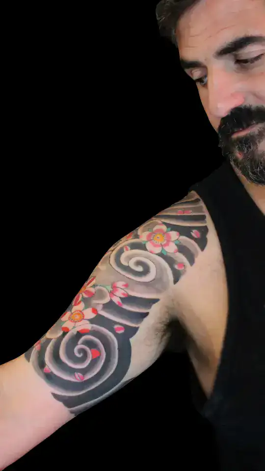 Tatuaje japonés de flores de cerezo y nubes en espiral recorriendo hombro y bíceps, composición sólida en negro y gris por Nikko Quiroga en Olivos.