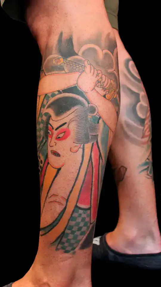 Tatuaje japonés de Sasaki Kojirou con katana alzada y rostro enmascarado en rojo, en el gemelo, estilo ukiyo-e por Nikko Quiroga.